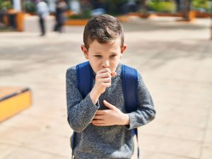 A young boy coughing outdoors, highlighting the impact of poor air quality on students' health and the need for regular air quality checks.